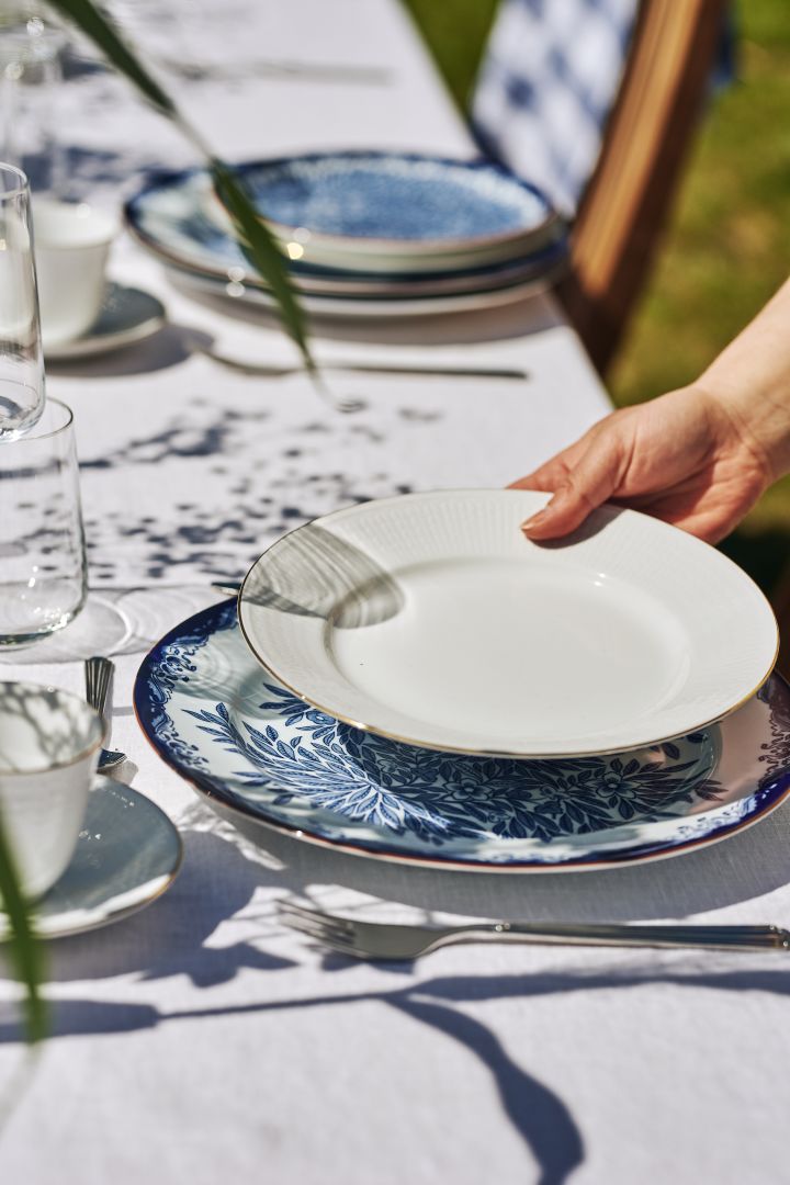 Perinteinen juhannuspöydän kattaus sinivalkoisin värein ruotsalaisella Grace Gala -lautasella, jossa on kultainen ääriviiva.