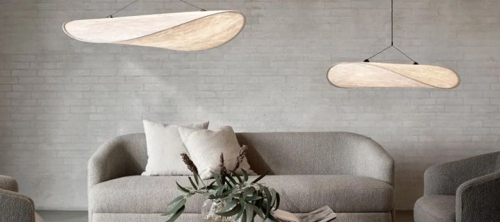 Näet kaksi merkin New Works Tense-lamppuvarjostinta roikkumassa harmaan sohvan ja sohvapöydän, jonka päällä on kirjoja, päällä. 