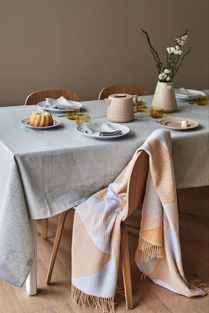 Vaaleankeltainen ja pastellinsininen NJRD Stripes -puuvillainen peitto peittää ruokapöydän tuolin.