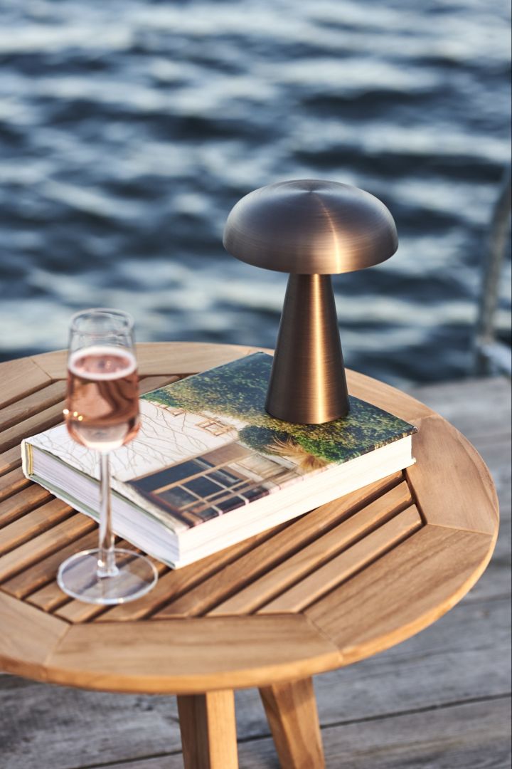 Johdoton pöytävalaisin Como merkiltä &Tradition, joka näkyy tässä puupöydällä viinilasillisen kanssa meren rannalla. 