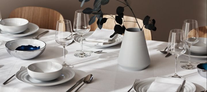 Viinilasit raikkaan valkoisella pöydällä, jossa on NRJD:n lautaset ja astiat. 