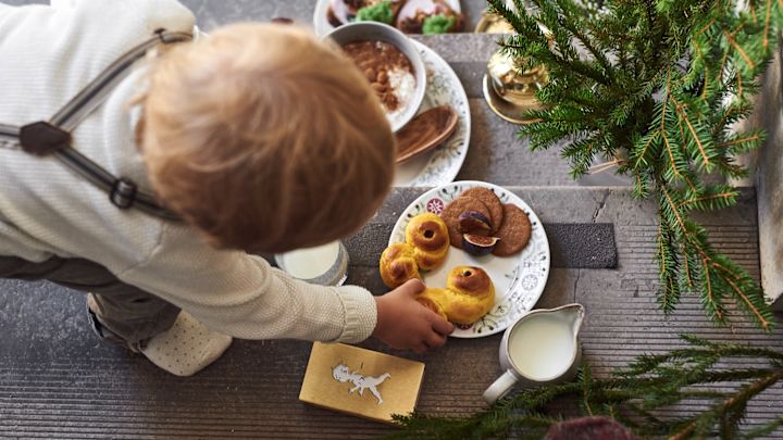 Tässä näet lapsen, joka kurottaa lussekattia Rörstrandin ruotsalaisen Grace Winter -malliston lautaselta.