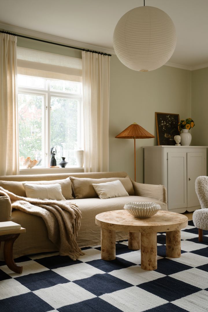 Kuvassa HAY:n Rice-paperilampunvarjostin roikkuu olohuoneessa, jossa on beige sohva, mustavalkoruutuinen matto ja rustiikkinen puinen sohvapöytä.