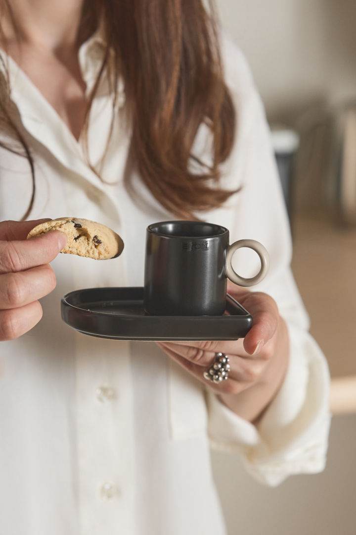 Tässä näet naisen, jonka toisessa kädessä on Byonin Niki-espressokuppi ja toisessa biscotti.