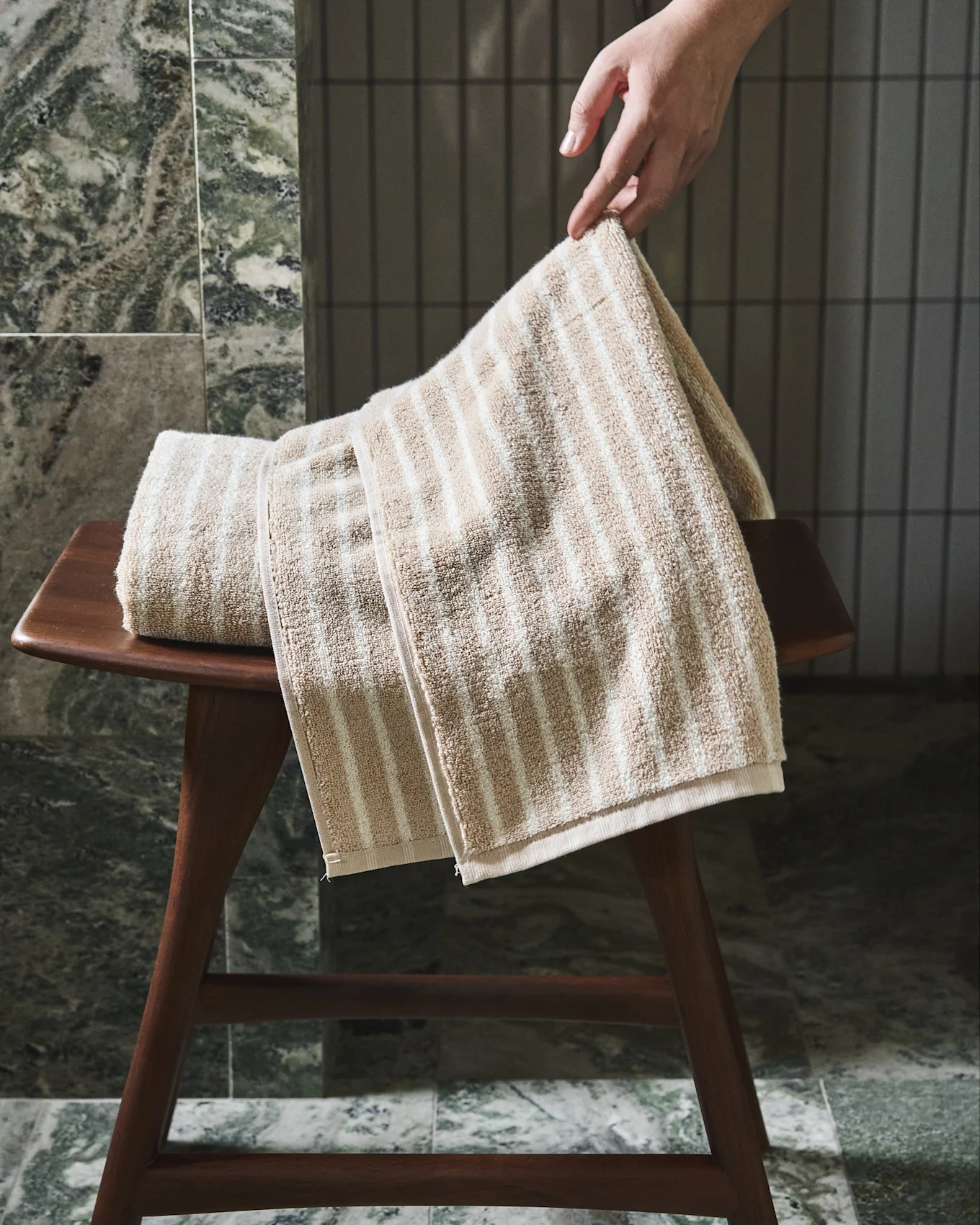 Käsi asettaa beige-valkoraitaisen pyyhkeen puiselle jakkaralle.