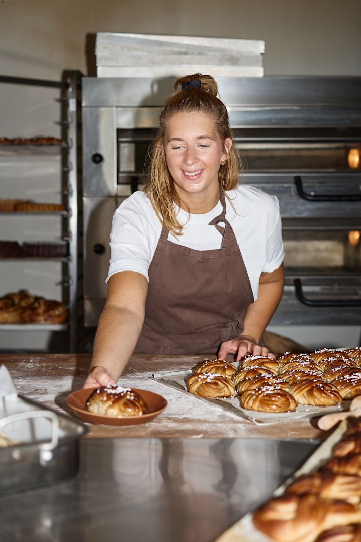 Tässä näet Lilian Sagerforsin leipomossaan Ekenäsissä esittelemässä valmiita kanelipullia Iittalan ruskealla Teema-lautasella, jolla hän voitti kultaa Ruotsin leipomomestaruuskilpailuissa.